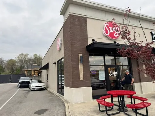 The first Swig Fund 2 store, a brick-and-stucco Swig shop with red patio tables